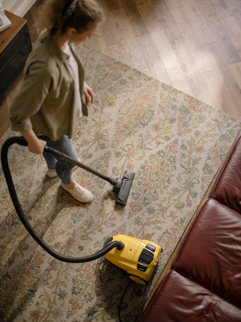 A professional cleaner from Slade Green Carpet Cleaners dressed in a white protective suit, gloves, face mask, and shoe covers is performing deep cleaning or sanitisation of a beige rectangular carpet
